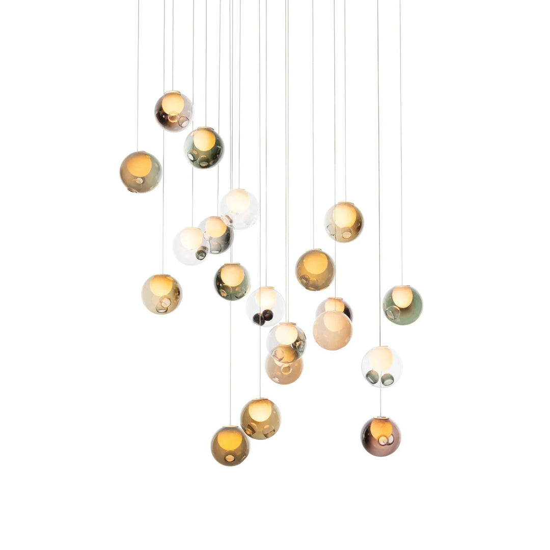 A chandelier with glowing glass globes in amber, green, pink, and clear finishes hangs at staggered heights against white.