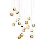 A chandelier with glowing glass globes in amber, green, pink, and clear finishes hangs at staggered heights against white.