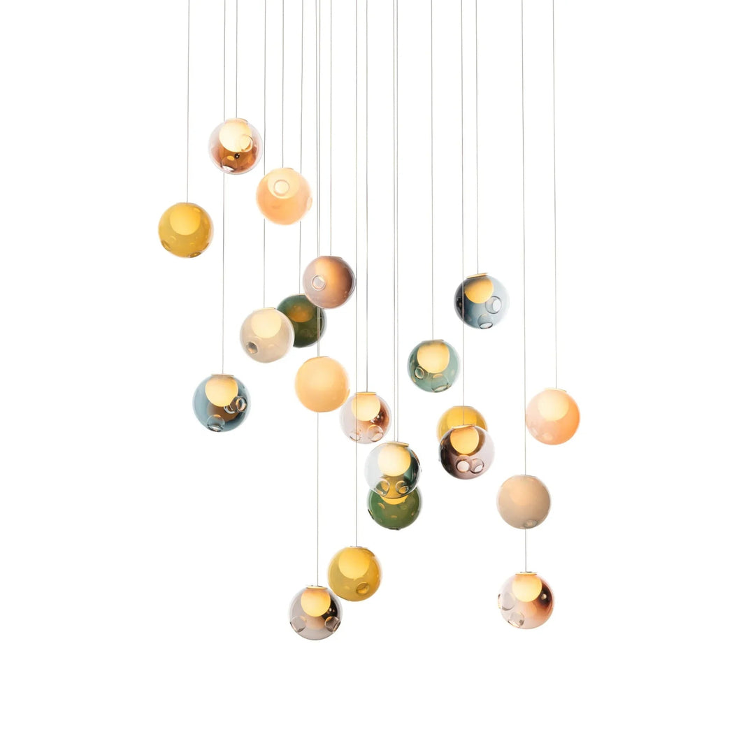 Illuminated chandelier with multicolored glass globes and glowing yellow centers hanging at staggered heights against a white background.
