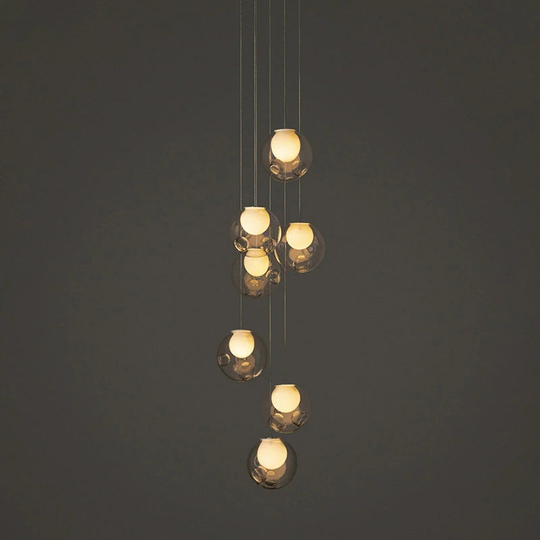 A modern multi-light pendant chandelier with seven clear glass bubble globes of varying sizes, suspended by thin cables against a dark gray background.