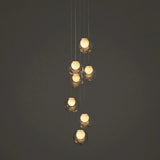 A modern multi-light pendant chandelier with seven clear glass bubble globes of varying sizes, suspended by thin cables against a dark gray background.