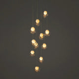 A modern multi-light pendant chandelier with clear faceted glass globes and warm glowing bulbs, suspended against a dark gray background.