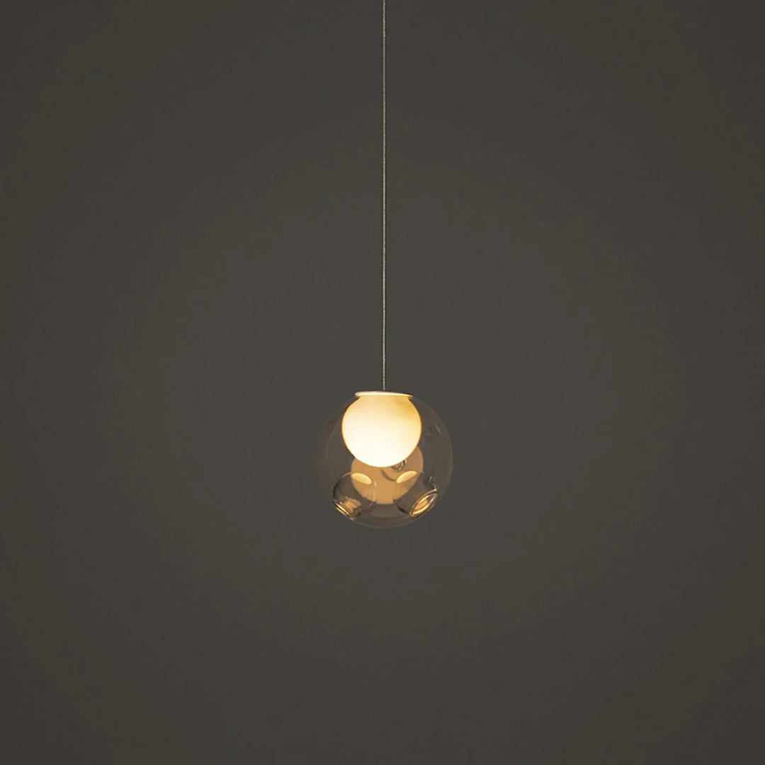 Single-light chandelier with a clear glass globe and glowing cream-colored inner shade hangs against a dark gray background.