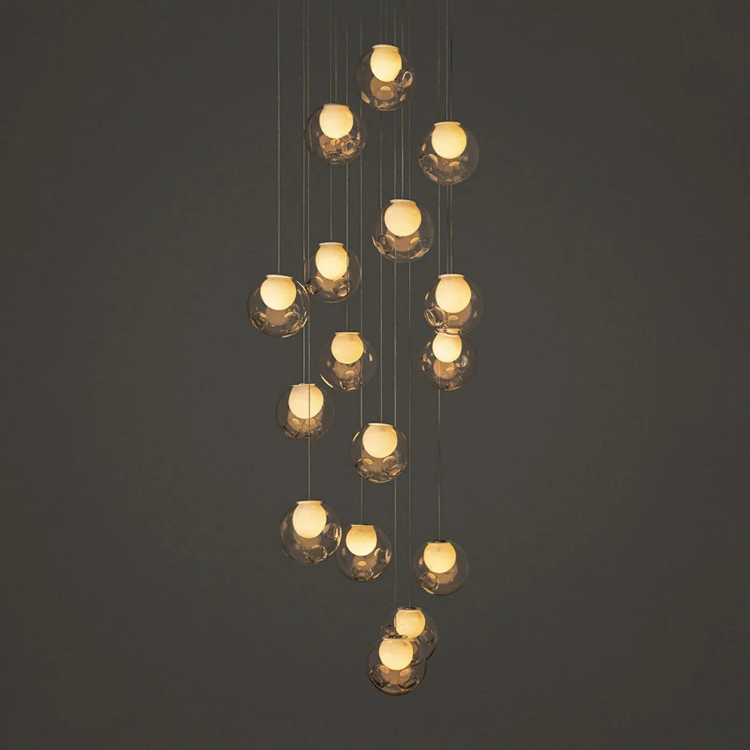 A modern multi-light pendant chandelier with multiple faceted clear glass globes suspended at varying heights against a dark gray background.