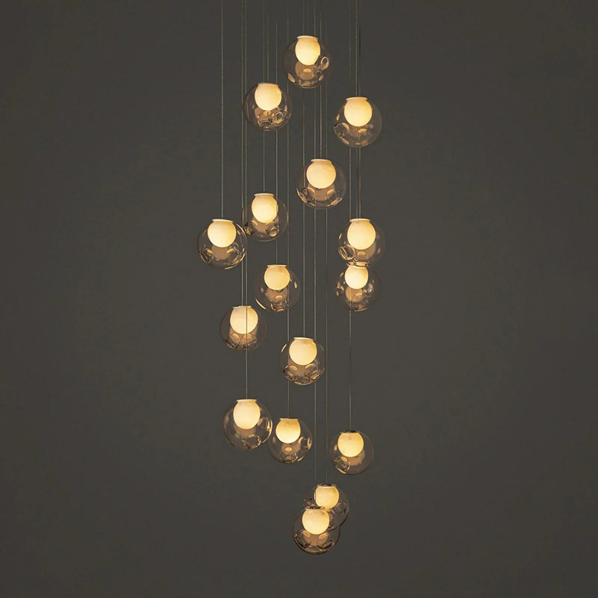 A modern multi-light pendant chandelier with multiple faceted clear glass globes suspended at varying heights against a dark gray background.