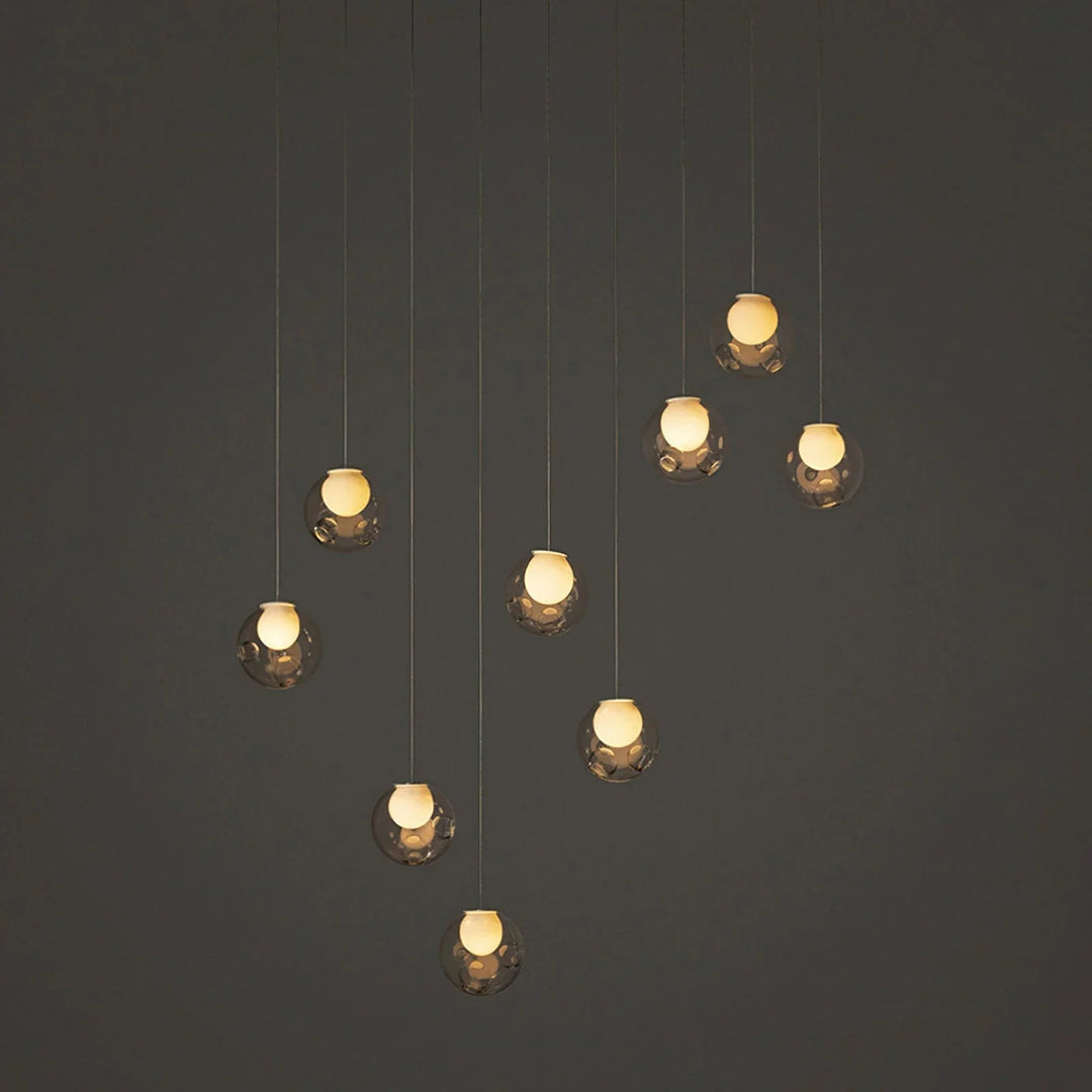 A modern multi-light pendant chandelier with nine clear glass globes suspended at varying heights against a dark gray background.