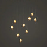 A modern multi-light pendant chandelier with nine clear glass globes suspended at varying heights against a dark gray background.