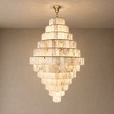 A tiered chandelier made of stacked rectangular stone slabs in warm beige and cream tones, hanging from a gold-toned ceiling canopy against a textured beige wall.