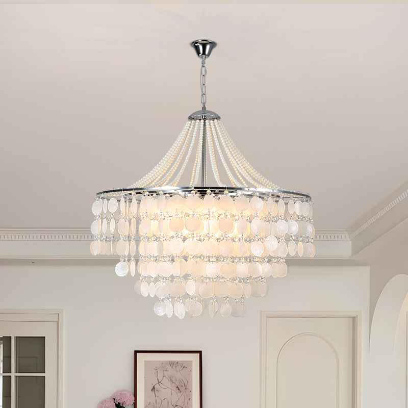 A multi-tiered chandelier with a silver-toned metal frame and cascading white crystal disc drops, hanging from the ceiling in a bright, modern room.