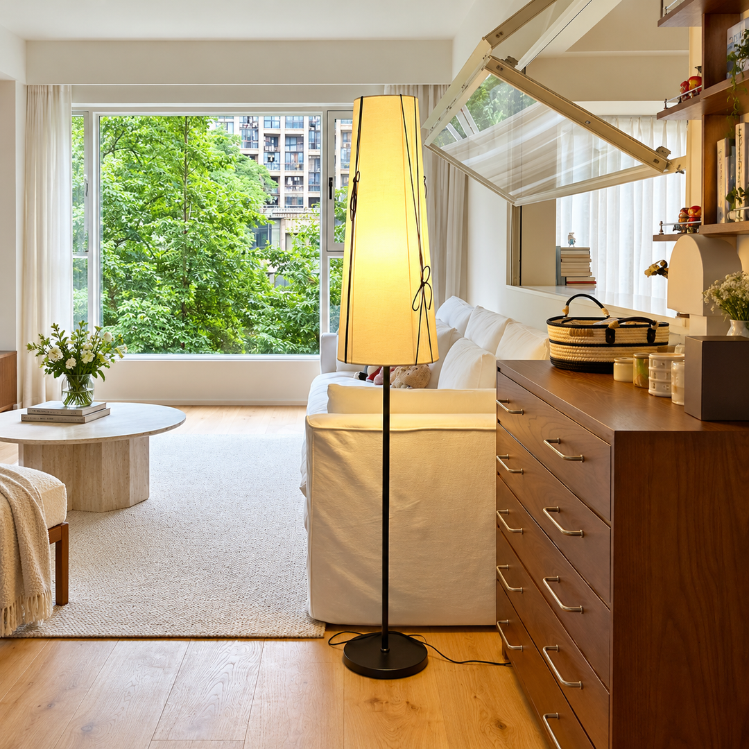 A modern floor lamp with a tall rectangular beige shade and black stand is positioned in a bright, contemporary living room next to a white sofa and wooden furniture.