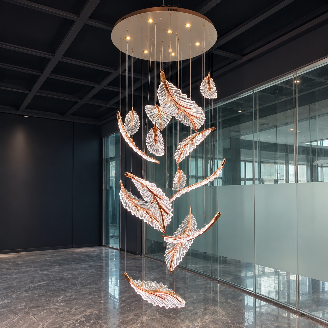 A modern multi-light feather chandelier with clear crystal-like leaves and warm copper-toned metal accents, suspended from a circular ceiling fixture in a contemporary office lobby with glass walls and a dark ceiling.