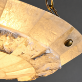 Detail of the semi-flush ceiling light showing illuminated alabaster veining, a brass fastener, and part of a chain against gray.