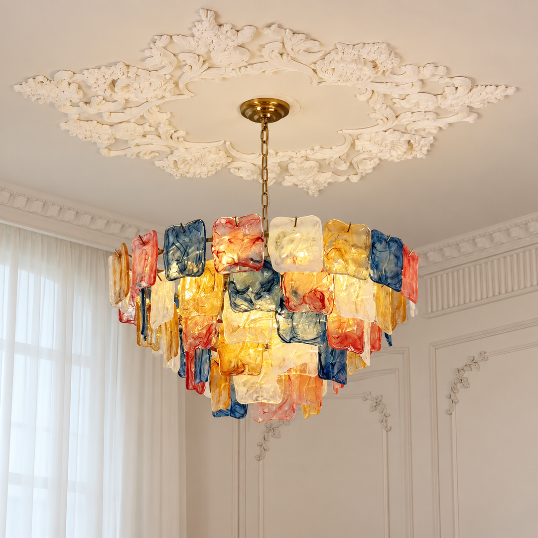 A decorative chandelier with layered translucent rectangular glass panels in blue, red, orange, yellow, and white, hanging from a gold-toned chain beneath an ornate white ceiling medallion.