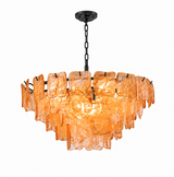 A modern tiered chandelier with a dark metal frame and hanging chain, featuring multiple overlapping translucent amber-orange glass panels that glow when lit, shown against a plain white background.