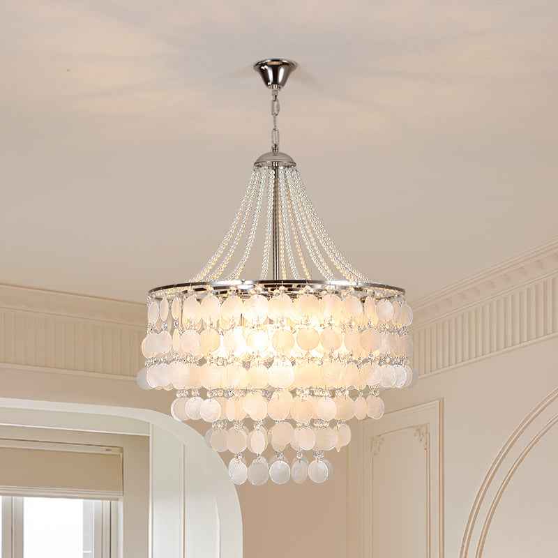 A multi-tiered crystal chandelier with a silver-toned metal frame and hanging glass beads, illuminated in a warm light, shown hanging from a ceiling in an elegant interior room.