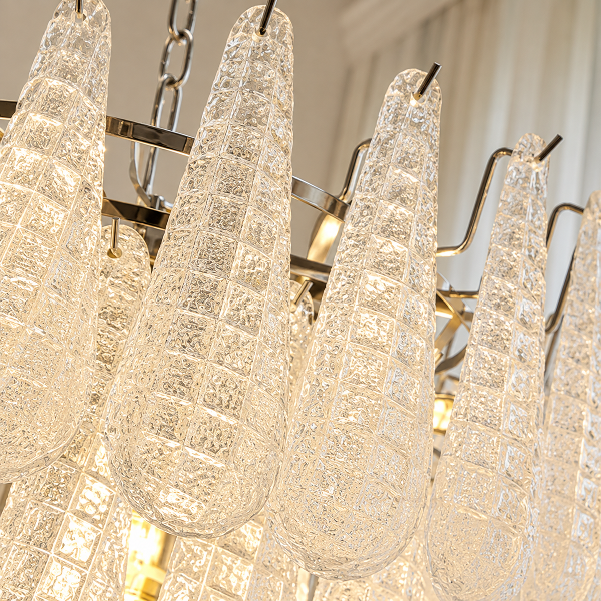 A close-up of a modern chandelier with textured, crackle-clear glass cone-shaped shades hanging from a polished brass or gold-toned metal frame.