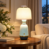 A table lamp with a ribbed white shade and a light blue and navy ceramic base with gold trim, placed on a wooden table in a cozy living room setting.