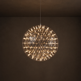Globe pendant light with an open geometric metal frame and warm glowing tubes hangs against a dark brown background.
