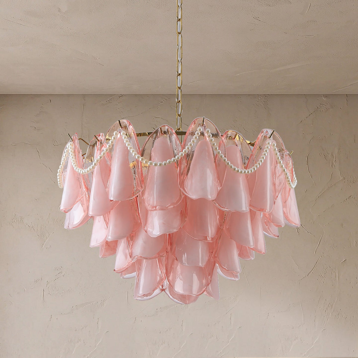 Tiered pink glass petal chandelier with draped white beads and a gold-tone suspension chain against a textured beige wall.