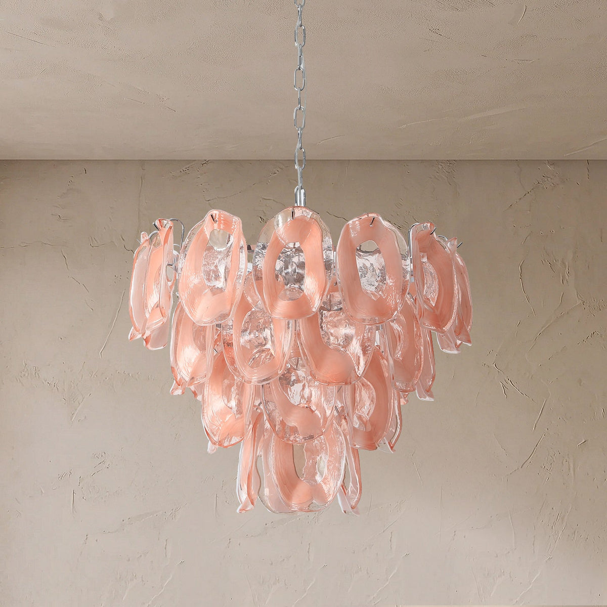 Tiered chandelier with pink and clear glass loops hangs from a silver chain against a textured beige wall.