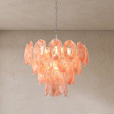 A modern cluster chandelier with translucent peach-pink glass petal-like shades hanging from a silver chain against a textured beige wall and ceiling.