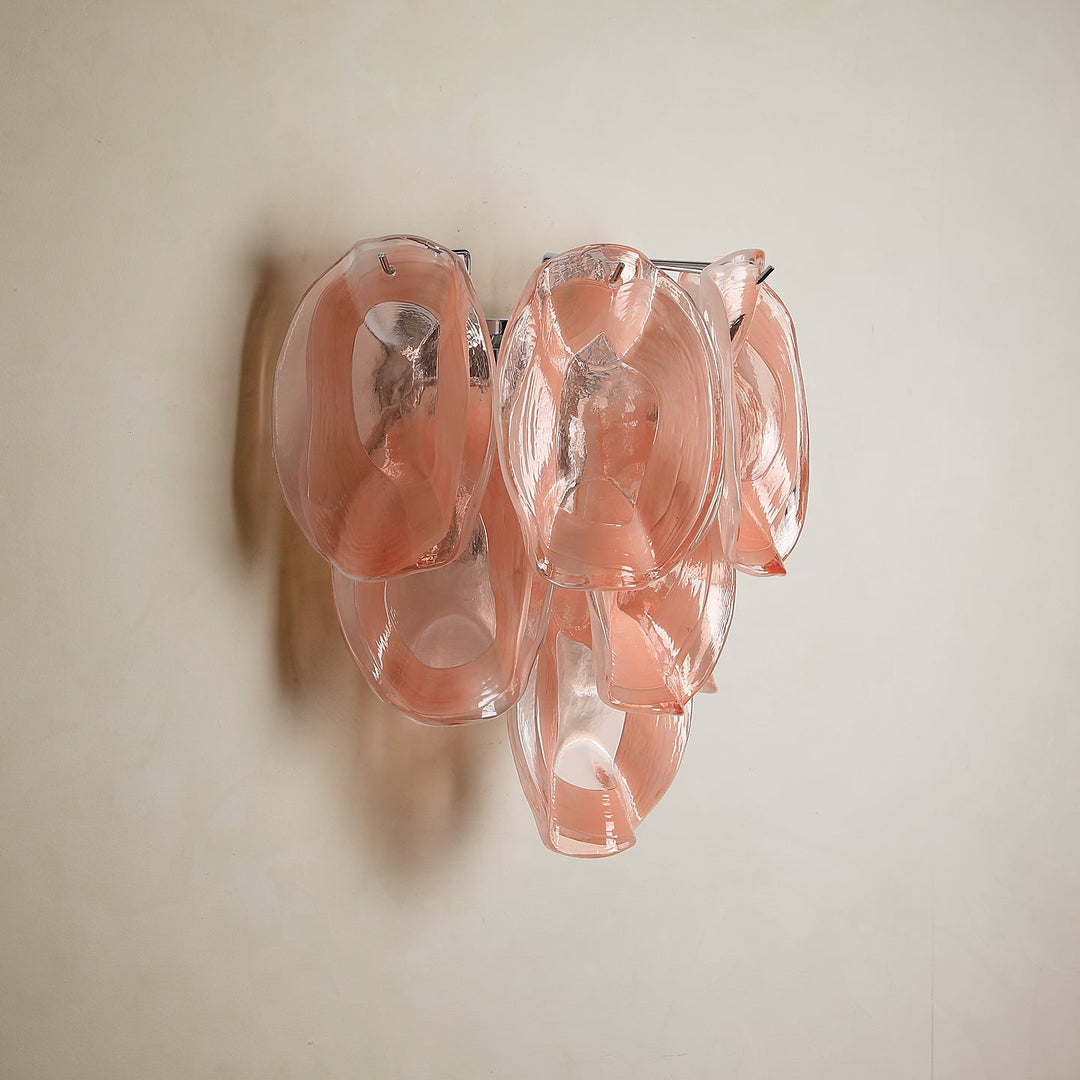 Wall sconce with overlapping translucent pink glass petals and visible metal supports mounted on a plain cream wall.