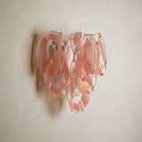 Wall sconce with overlapping translucent pink glass petals and visible metal supports mounted on a plain cream wall.