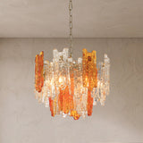 A modern chandelier with amber and clear glass rod accents hanging from a chain against a textured plaster wall.