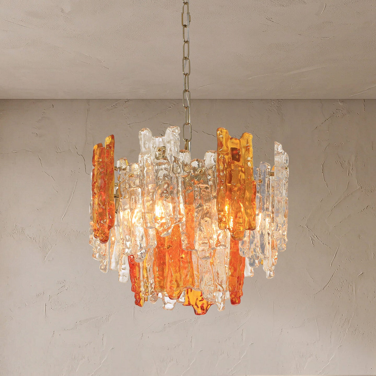 A modern chandelier with amber and clear glass rod accents hanging from a chain against a textured plaster wall.