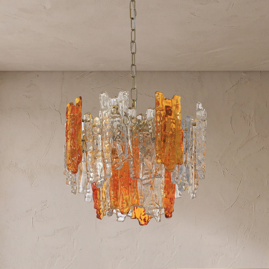 Chandelier of amber orange and clear textured glass panels hanging from a chain against a beige plastered wall