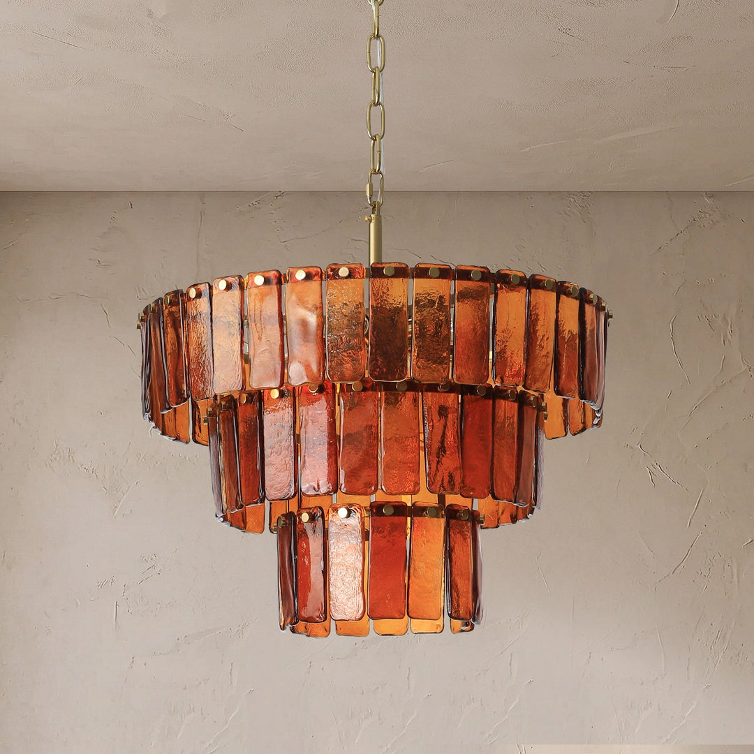 Three-tier chandelier with amber rectangular glass panels and a gold-tone suspension chain against a textured beige wall.
