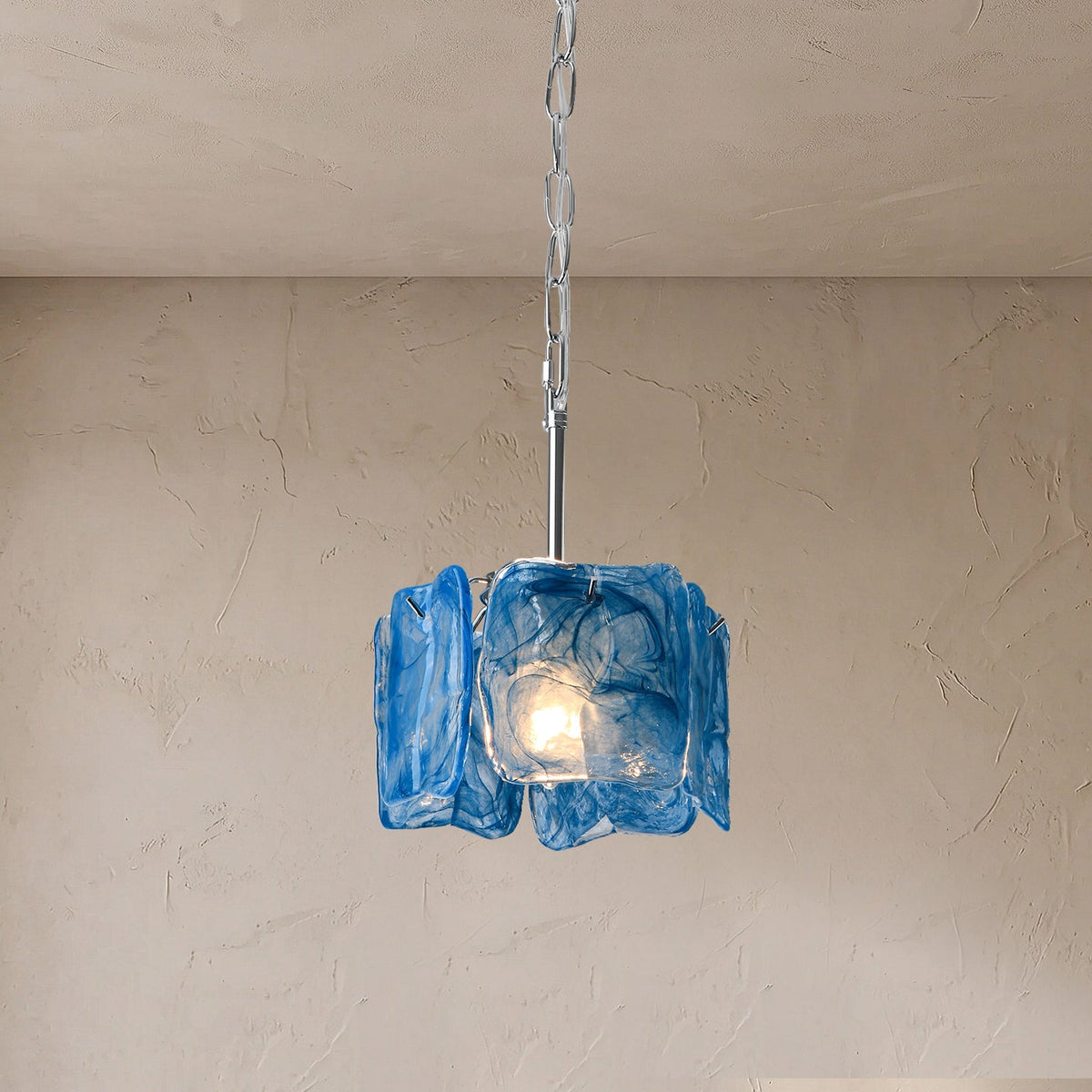 A hanging pendant light with a textured blue glass shade and a silver metal chain, shown against a beige plaster wall and ceiling.
