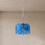 A blue textured glass pendant light hanging from a silver metal rod and chain against a beige plaster wall and ceiling.