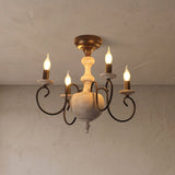 A rustic five-light chandelier with a distressed white wood central body and dark metal scroll arms, shown lit against a textured beige plaster ceiling and wall.