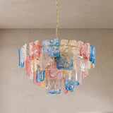 A modern chandelier featuring multiple rectangular glass shades in translucent white, pink, blue, and yellow, suspended from a gold chain against a textured beige wall and ceiling.