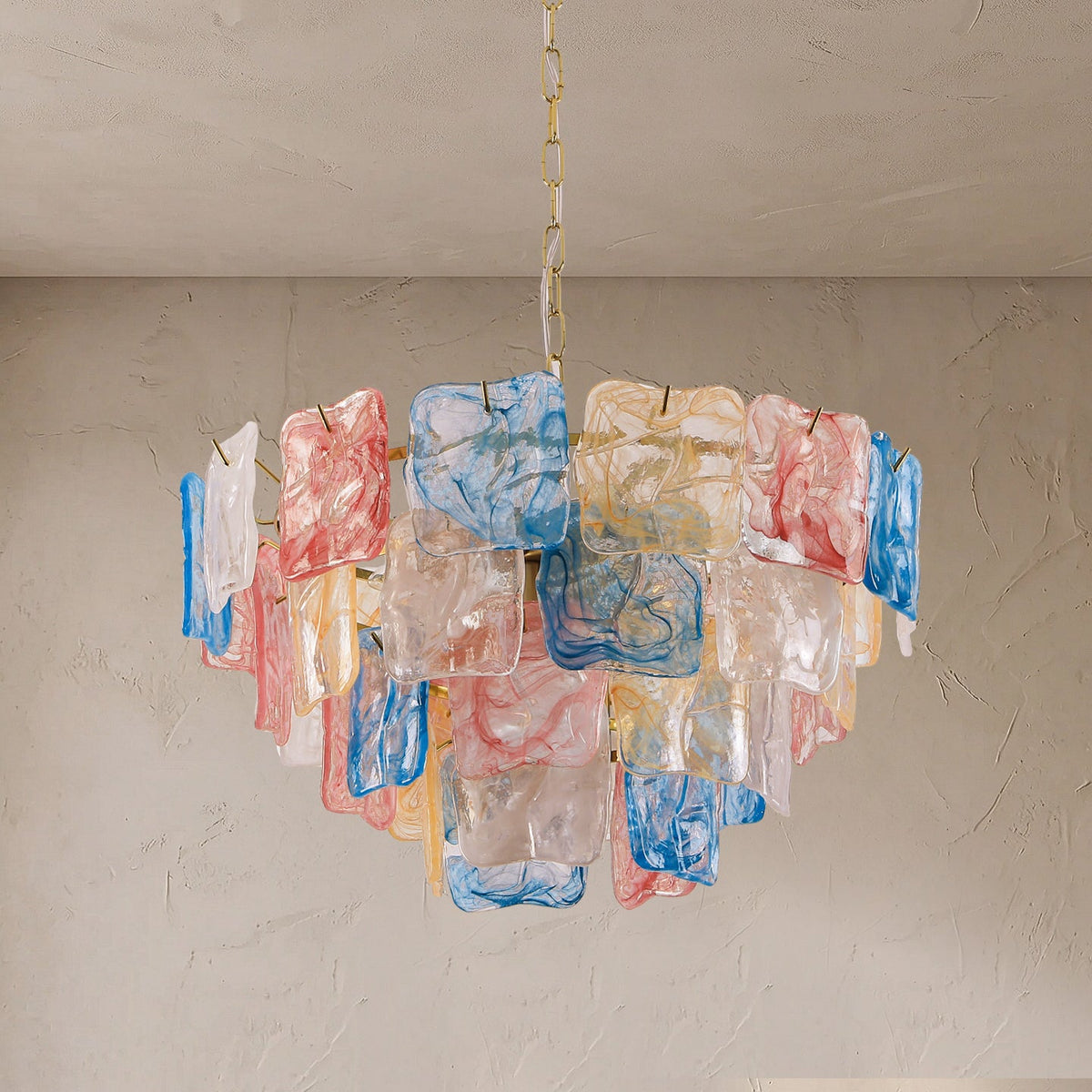 A modern chandelier featuring multiple rectangular glass shades in translucent white, pink, blue, and yellow, suspended from a gold chain against a textured beige wall and ceiling.