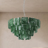 A green glass chandelier with multiple square-shaped translucent shades, suspended from a chain against a textured beige plaster wall and ceiling.