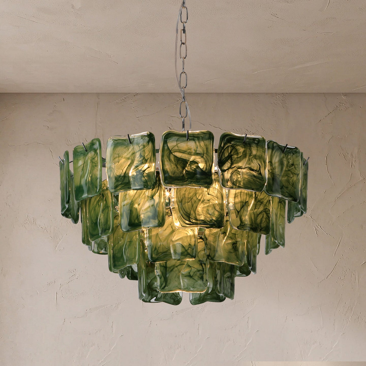 Illuminated chandelier with tiered green marbled glass panels hangs from a silver chain against a textured beige wall.