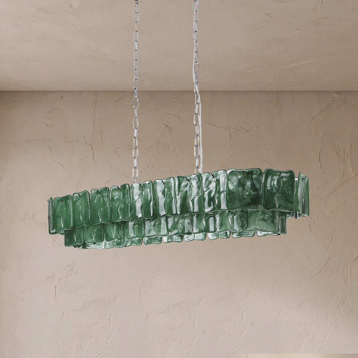 An unlit linear chandelier with two tiers of rippled green glass panels hangs from silver-toned chains against a beige wall.