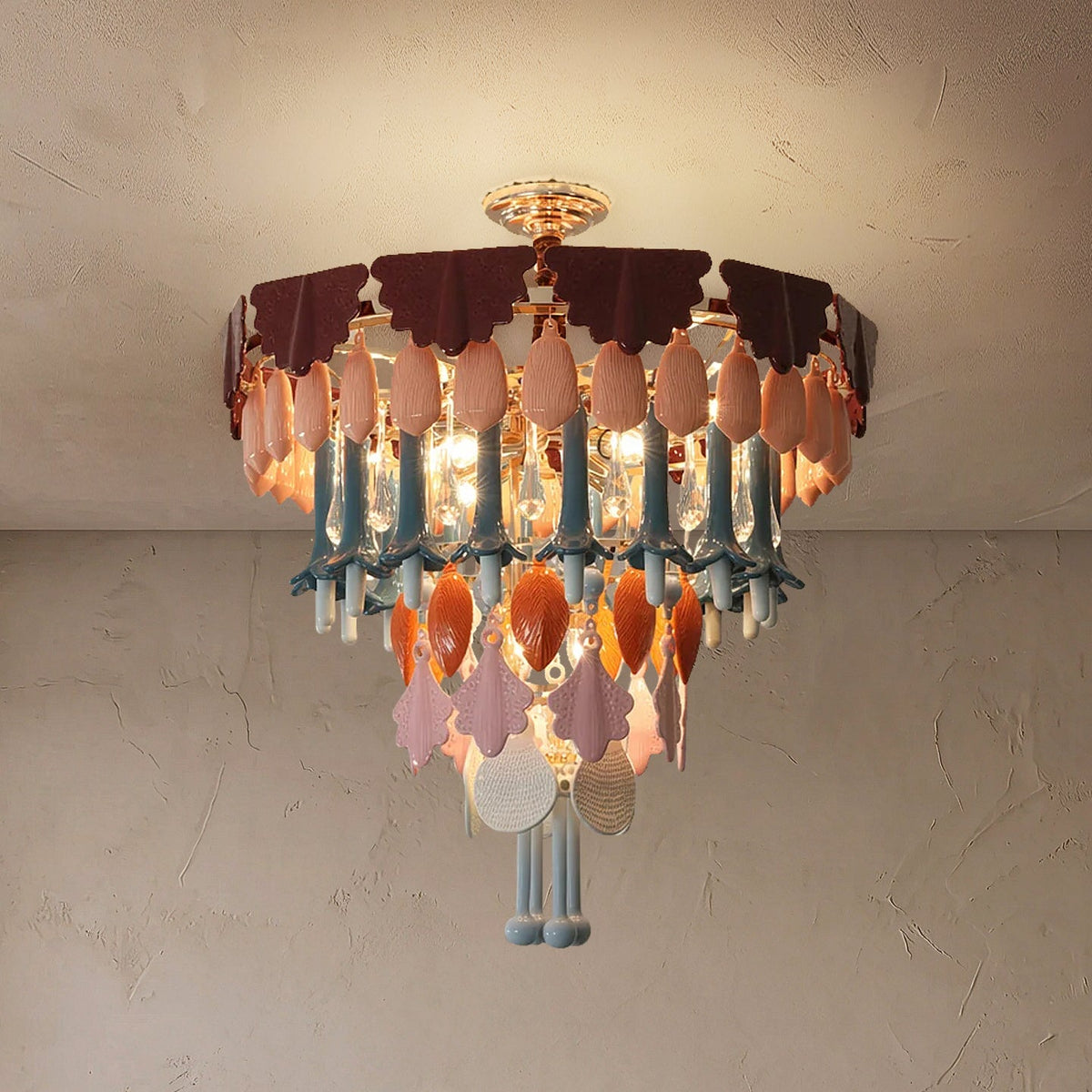 Illuminated chandelier with gold ceiling mount and tiered burgundy, pink, blue, and orange decorative pendants against a textured beige ceiling.