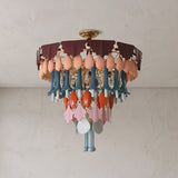 Round chandelier with burgundy scalloped pieces and peach, blue, orange, and clear glass drops against a white ceiling.