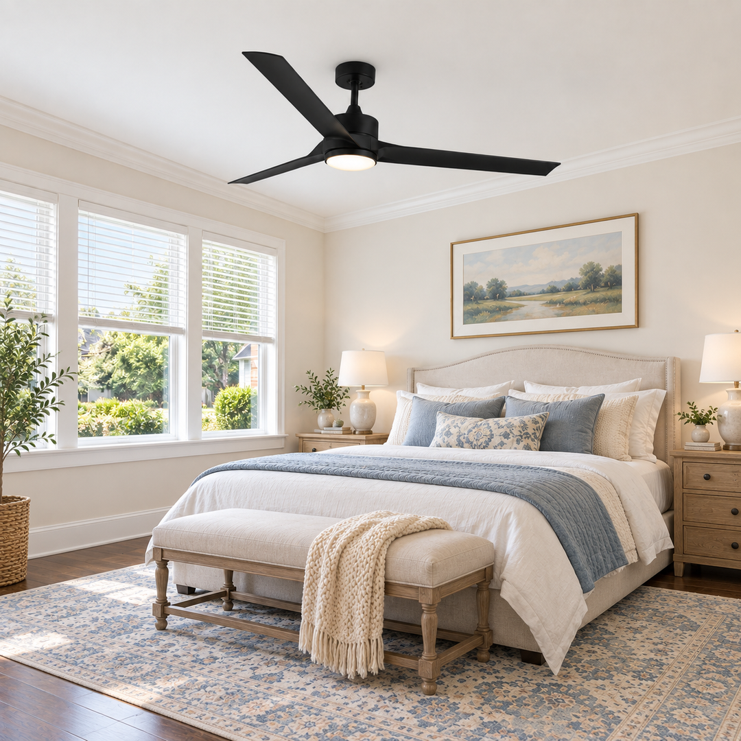 A modern black ceiling fan with a light fixture is mounted on a white ceiling in a beautifully styled bedroom with beige walls, a bed with blue and cream bedding, and a patterned blue rug.