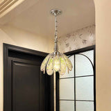 Glass petal chandelier with green accents glows warmly beside a dark door and black-framed textured glass window.