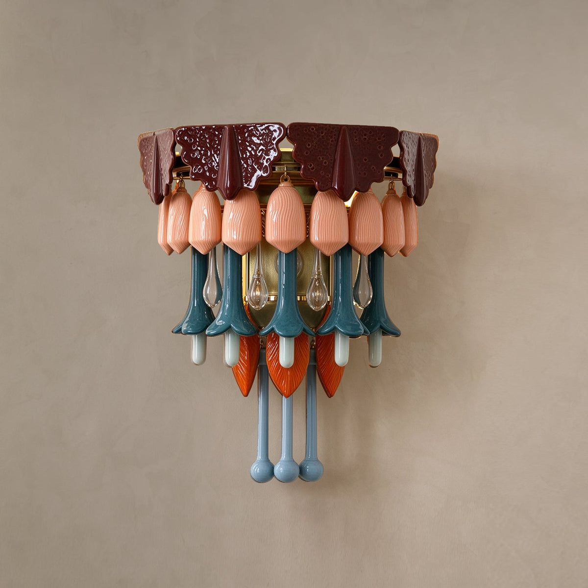 A multicolored ceramic and glass wall sconce with a burgundy top, peach shades, and teal, orange, and blue hanging drops on a beige wall.