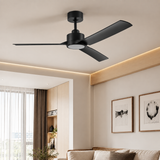 A matte black three-blade ceiling fan with a light diffuser, mounted on a beige ceiling in a modern, minimalist living room with warm ambient lighting.