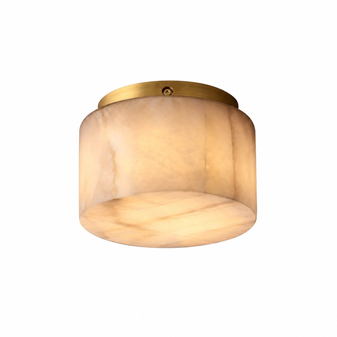A modern semi-flush mount ceiling light featuring a warm, glowing oval-shaped translucent shade made of cream-colored stone, mounted on a brushed brass circular ceiling canopy.