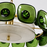 A close-up of a modern chandelier featuring textured green glass shades with a gold metal frame and a clear ribbed glass diffuser plate.