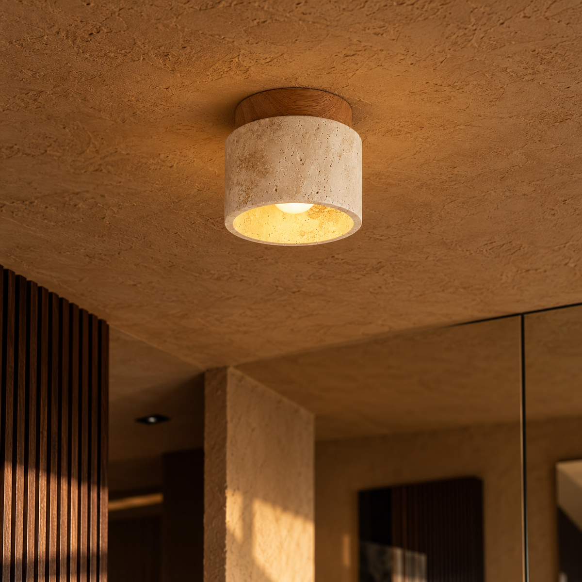 A modern semi-flush mount ceiling light fixture with a textured beige stone cylinder shade and a natural wood top cap, glowing with a warm yellow light in a textured plaster room.
