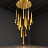 A modern multi-light chandelier pendant lamp with a circular gold top canopy and multiple vertical gold tubes of varying lengths, each ending in a small glowing bulb, suspended in a dark room.