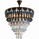 A tiered chandelier light fixture featuring blue glass teardrop beads, clear glass leaf-shaped prisms, and hanging glass tubes, suspended from a dark metal canopy against a white background.